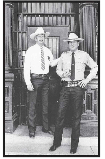 Sheriff Thompson in cowboy hat rests his hand on the shoulder of Texas Ranger Joaquin Jackson on the steps of the county jail.